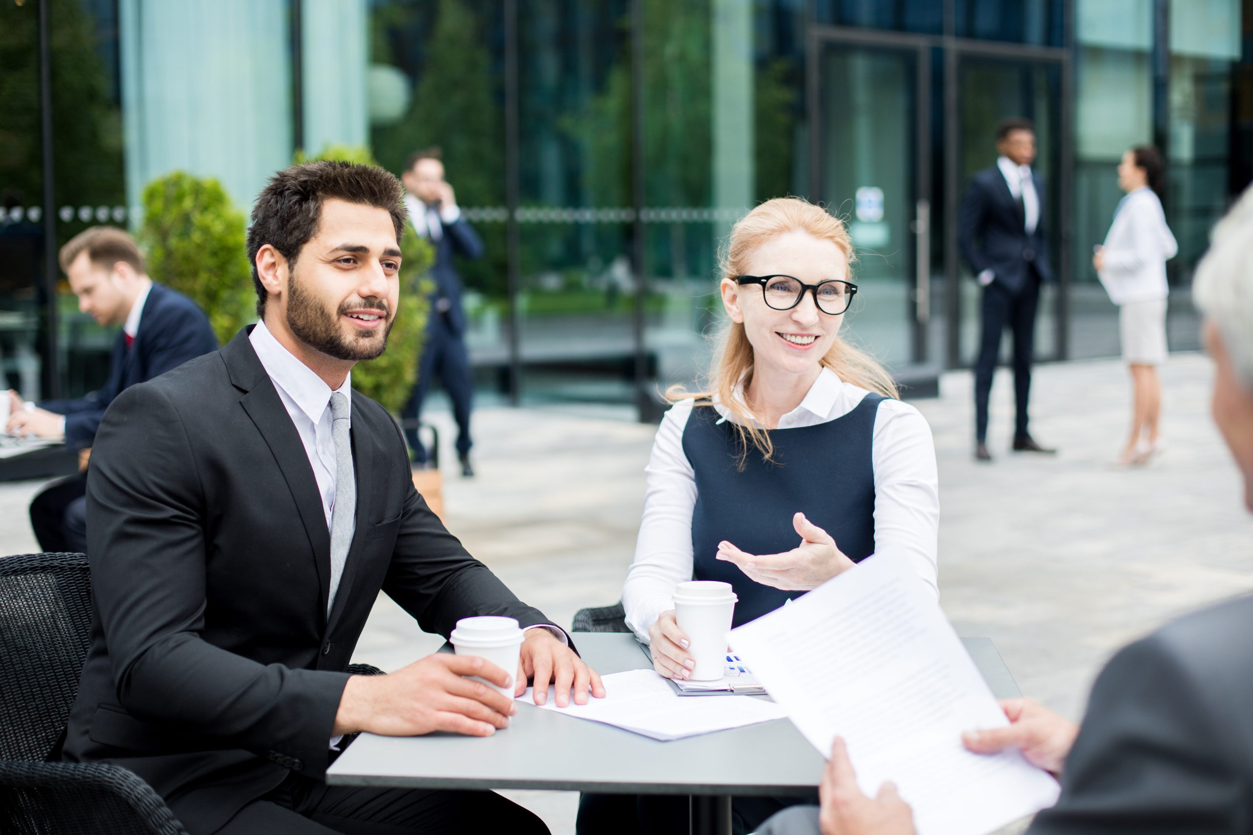 Two young colleagues having talk to foreign delegate and discussing financial questions